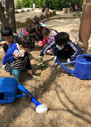 어린 아이들이 모두의 정원에 마련된 놀이터에서 모래를 가지고 노는 모습